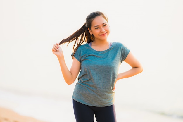 Funcionamiento y ejercicio asiáticos de la mujer del deporte joven hermoso del retrato en la playa cerca del mar y del océano en el tiempo de la salida del sol o de la puesta del sol