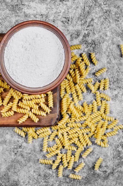 Fusilli crudo y un cuenco de harina sobre la mesa de mármol.