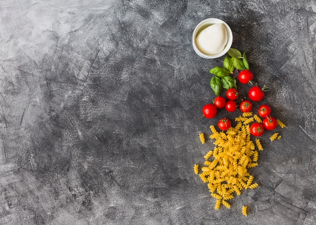 Fusilli crudo con tomates cherry; hojas de albahaca; Pimienta negra y queso sobre fondo de textura