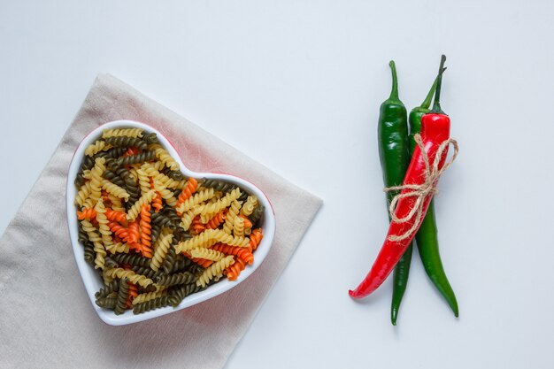 Fusilli pasta con pimientos en un recipiente sobre la mesa de mantel blanco y doblado, endecha plana.