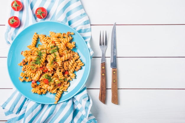 Fusilli de pasta con tomate y cubiertos en mesa de madera blanca