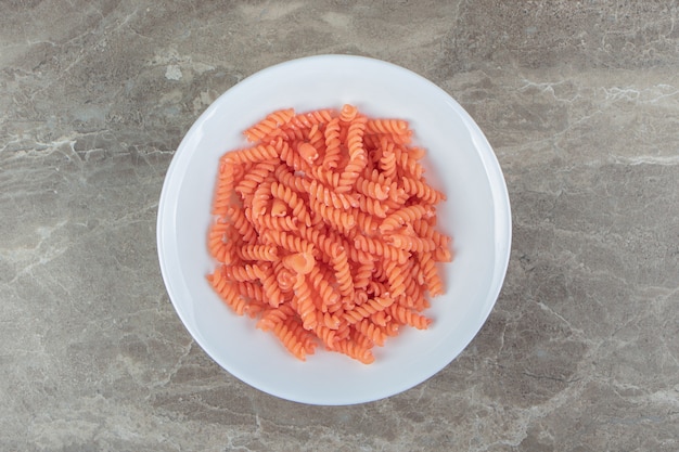 Fusilli rojo crudo en tazón de fuente blanco