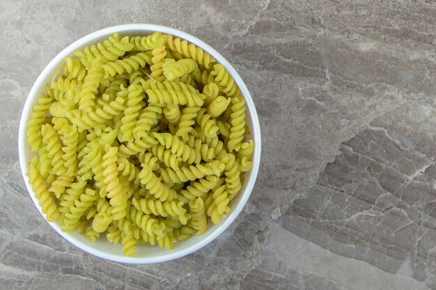 Fusilli verde crudo en tazón de fuente blanco.