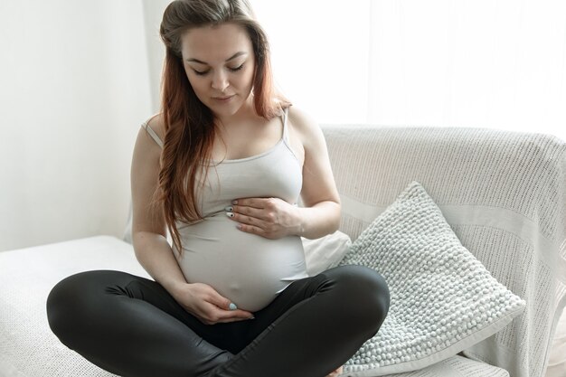 La futura madre con una gran barriga está sentada en el sofá de su casa.