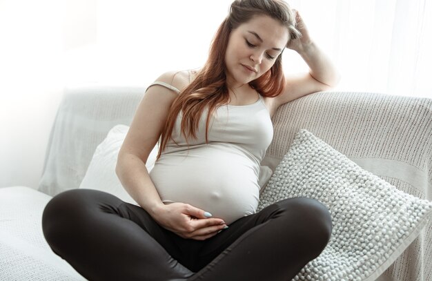 La futura madre con una gran barriga está sentada en el sofá de su casa.