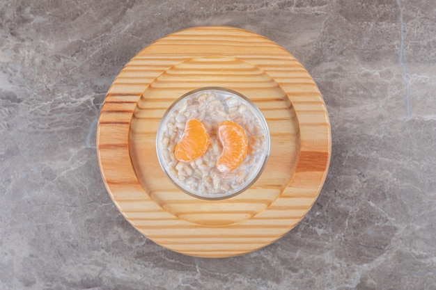 Foto gratuita gachas de avena con dos rodajas de naranja en un vaso sobre una placa de madera, sobre el fondo de mármol.