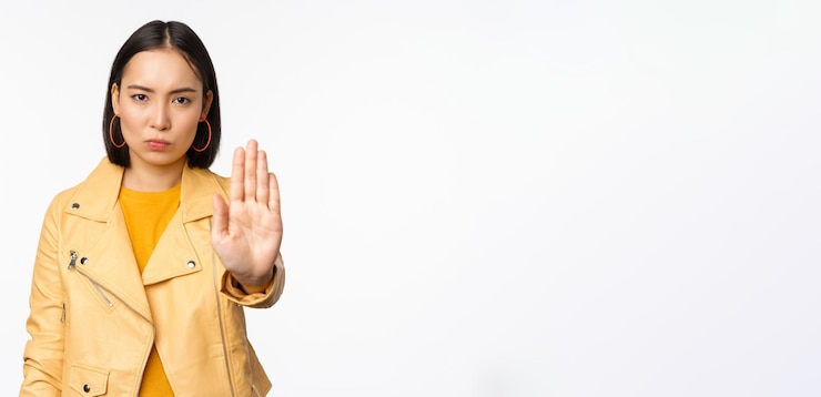 Photo Gratis gadis asia yang serius dan khawatir mengulurkan telapak tangan gestur berhenti melarang sesuatu melarang berdiri di atas latar belakang studio putih