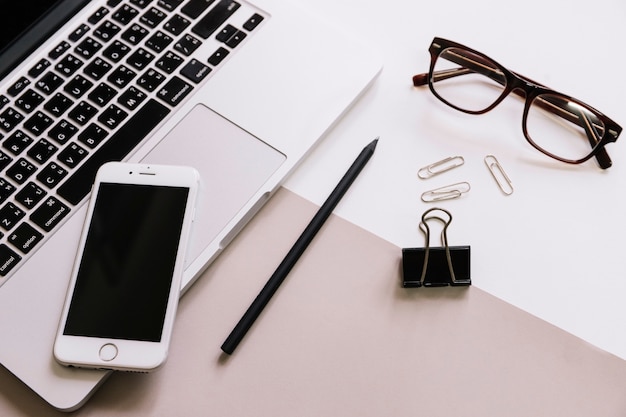 Gafas y artículos de papelería cerca de teléfono inteligente y computadora portátil