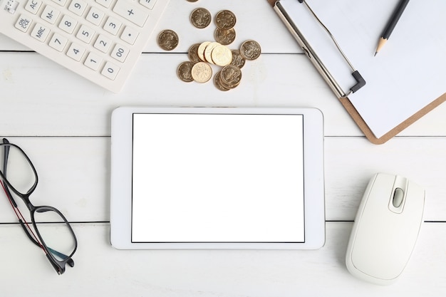 Gafas, calculadora, monedas y tableta en blanco escritorio aseado