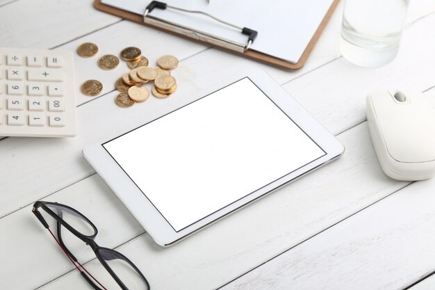 Gafas, calculadora, monedas y tableta en blanco escritorio aseado