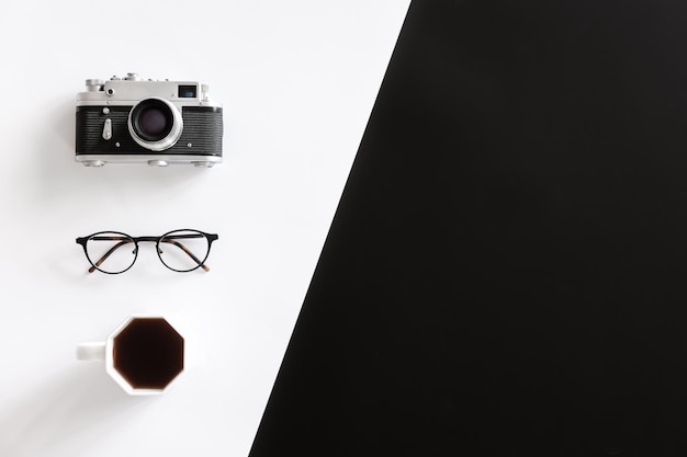 Gafas de cámara retro vintage y taza de café sobre fondo blanco y negro