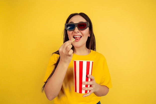 Gafas de cine 3D y palomitas de maíz. Retrato de mujer caucásica aislado en pared amarilla. Preciosa modelo de estilo casual. Concepto de emociones humanas, expresión facial, ventas, copyspace.