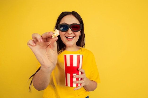 Gafas de cine 3D y palomitas de maíz. Retrato de mujer caucásica aislado sobre fondo amarillo de estudio. Preciosa modelo de estilo casual. Concepto de emociones humanas, expresión facial, ventas, anuncios, copyspace.