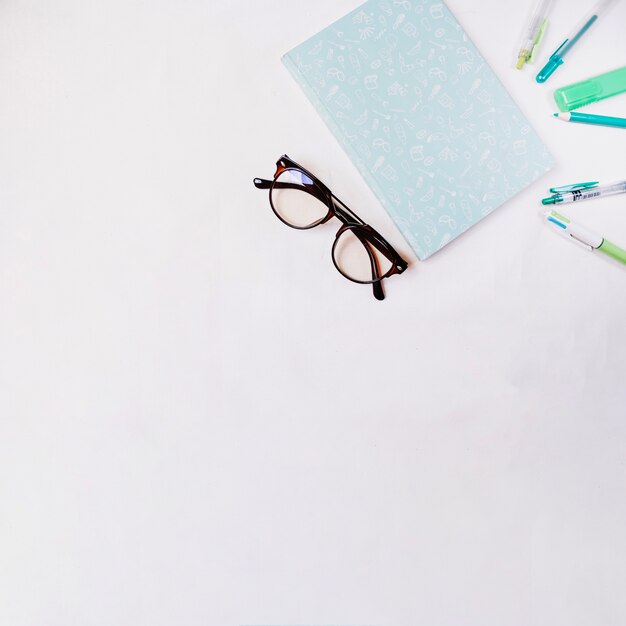 Gafas y cuaderno cerca de suministros de escritura