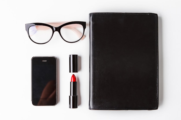 Gafas de lápiz labial rojo teléfono y portátil sobre fondo blanco.