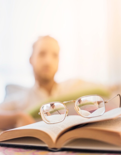 Gafas en libro con hombre borroso al fondo