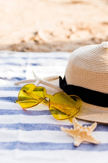 Foto gratuita gafas de sol de corazón amarillo, sombrero de paja y estrellas de mar en la toalla de playa en la playa