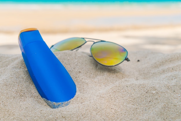 Gafas de sol y crema de protección solar en la playa de arena blanca