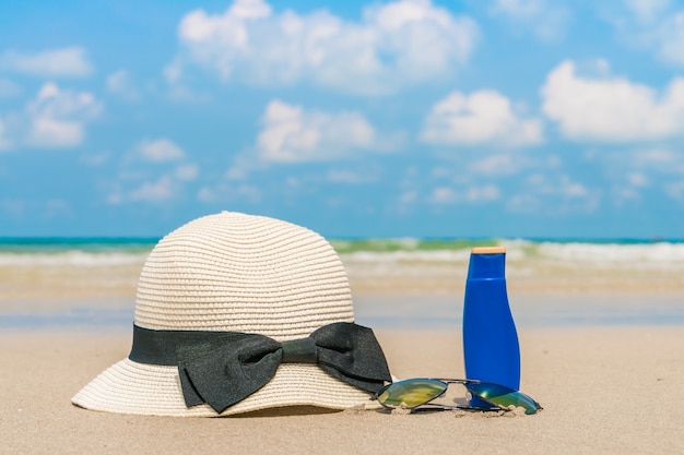 Gafas de sol, crema solar y sombrero en la playa de arena blanca