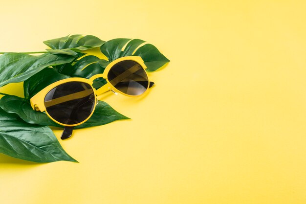 Gafas de sol con hojas verdes artificiales sobre fondo amarillo