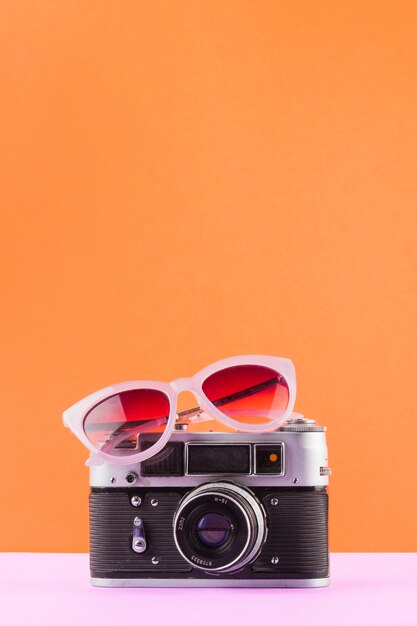 Gafas de sol sobre la cámara vintage en escritorio blanco sobre un fondo naranja