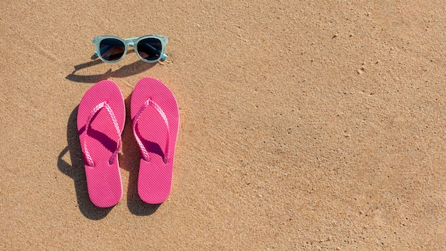 Gafas de sol y zapatillas de playa sobre arena.