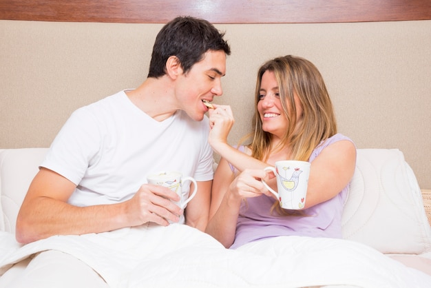 Foto gratuita galleta de alimentación de la mujer feliz a su novio que se sienta en cama