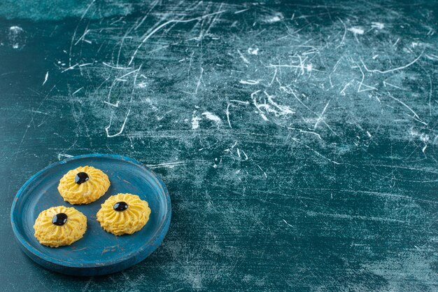 Galleta con chocolate en una placa de madera, sobre fondo azul. Foto de alta calidad