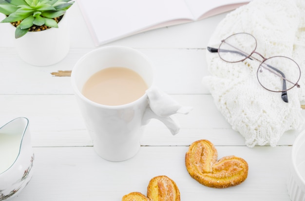 Foto gratuita galleta de hojaldre palmiers con taza de té de porcelana blanca en el escritorio de madera