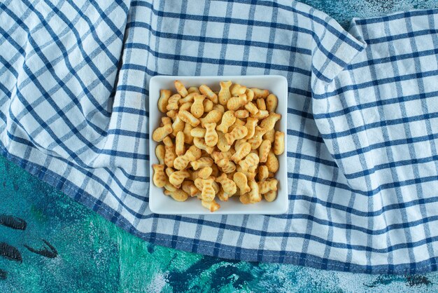 Galleta de pescado en un recipiente sobre un paño de cocina, sobre la mesa azul.