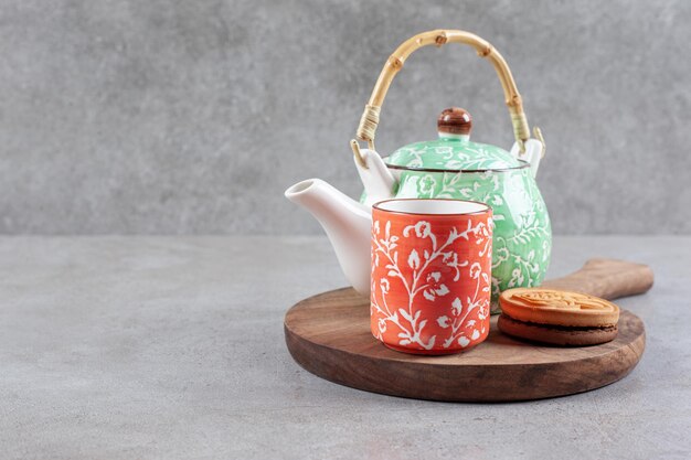 Una galleta, una taza de té y una tetera sobre tabla de madera sobre fondo de mármol. Foto de alta calidad