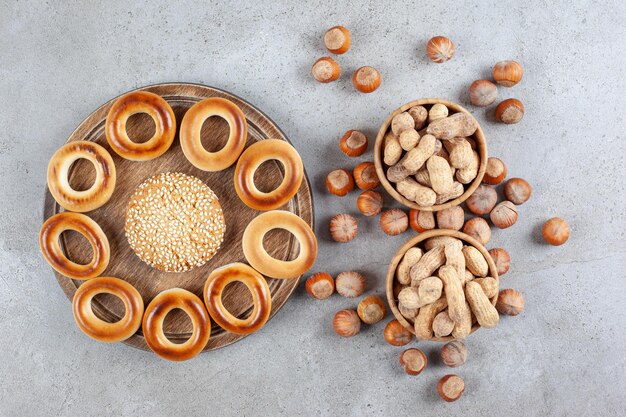 Galleta única rodeada de sushki sobre una tabla de madera junto a cuencos de maní y avellanas esparcidas sobre fondo de mármol. Foto de alta calidad