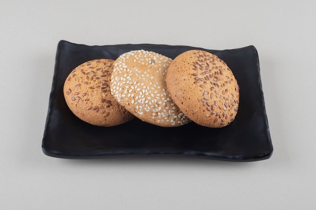 Galletas agrupadas en un plato negro sobre fondo de mármol.