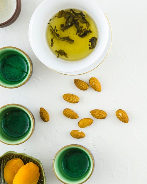 Galletas; Almendras con té de hierbas y tazas sobre fondo blanco con textura