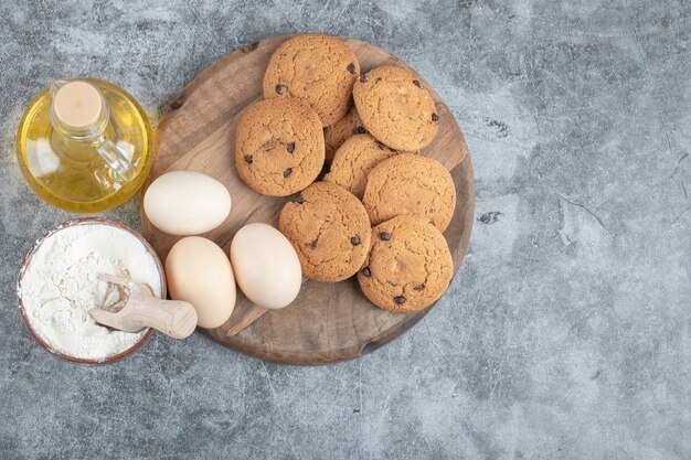 Galletas de avena con gotas de chocolate sobre una tabla de madera con ingredientes alrededor