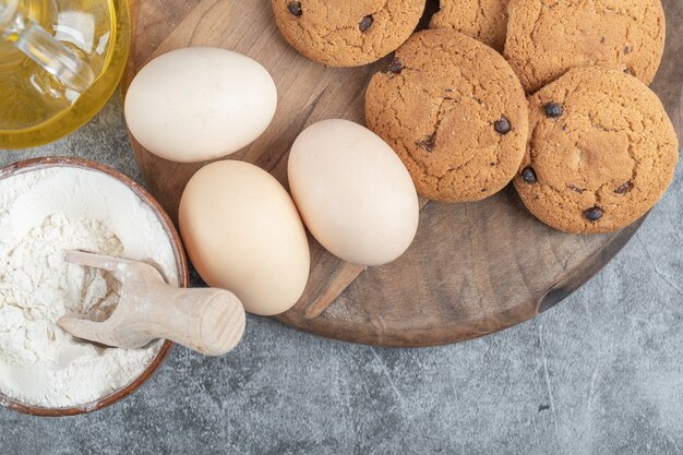 Galletas de avena con gotas de chocolate sobre una tabla de madera con ingredientes alrededor