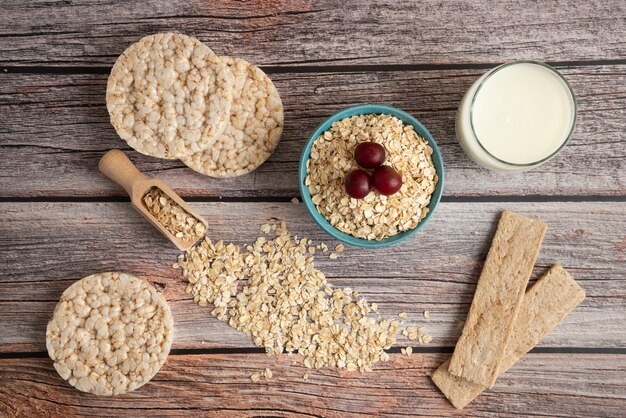 Galletas de avena, granos con bayas y una taza de leche en la mesa, vista superior