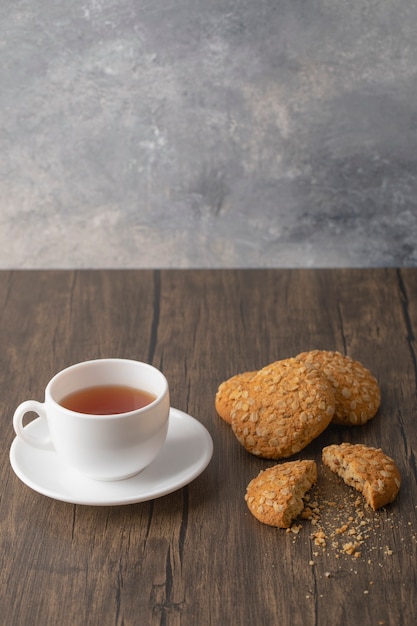 Galletas de avena con semillas y cereales cerca de una taza blanca de té negro