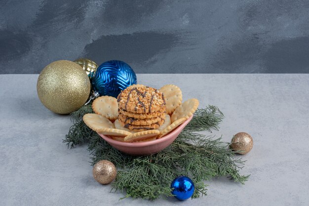 Galletas y bizcochos en un recipiente en medio de adornos navideños en la superficie de mármol