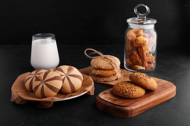 Galletas con cacao, sésamo y comino con un vaso de leche sobre fondo negro.