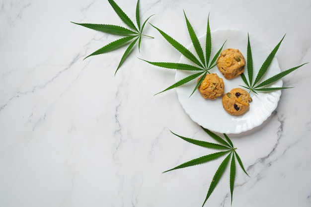 Galletas de cannabis y hojas de cannabis en placa blanca.