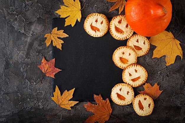 Galletas caseras en forma de calabazas de Halloween Jack-o-lantern en la mesa oscura. Vista superior.