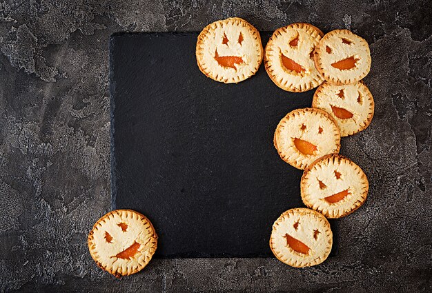 Galletas caseras en forma de calabazas de Halloween Jack-o-lantern en la mesa oscura. Vista superior.