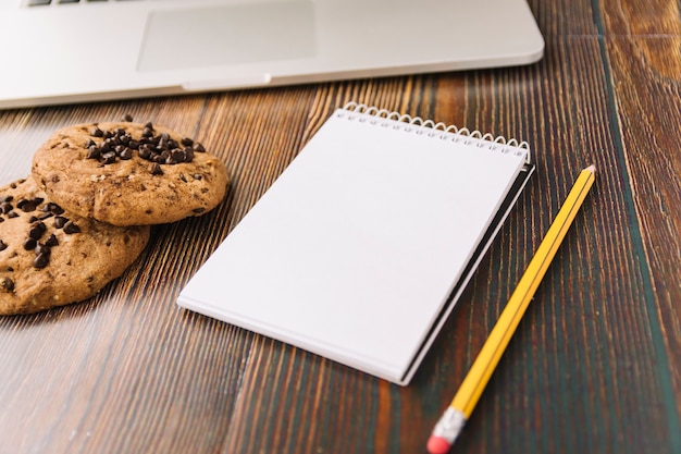 Foto gratuita galletas cerca del cuaderno con lápiz y computadora portátil