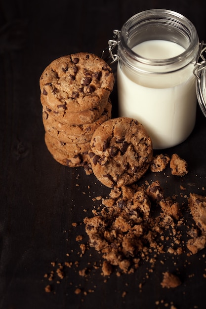 Galletas de chispas de chocolate caseras con botella de leche y migas en la mesa de madera rústica. Postre dulce.