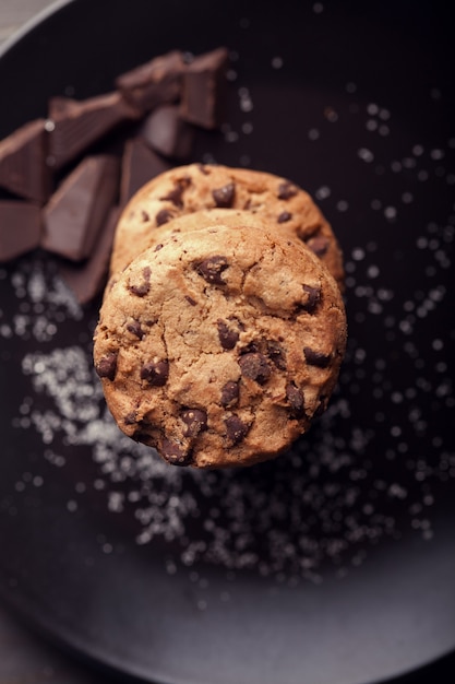 Galletas con chispas de chocolate en placa negra. Mesa de madera vieja oscura.