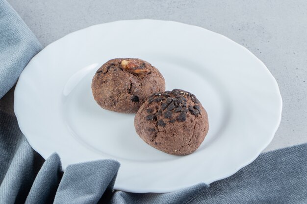 Galletas con chispas de chocolate en un plato blanco junto al mantel sobre fondo de mármol.