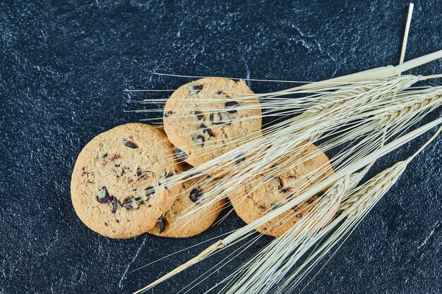 Galletas de chispas de chocolate sobre una superficie de mármol con espigas de trigo