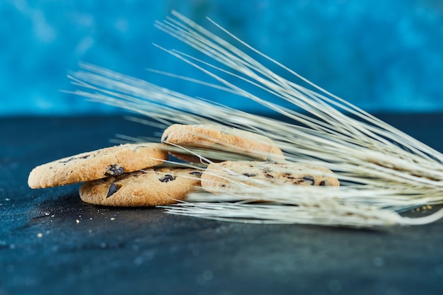 Galletas de chispas de chocolate sobre una superficie de mármol con espigas de trigo