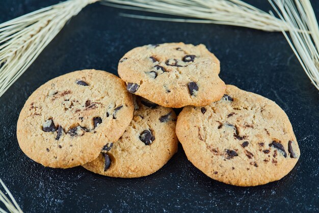 Galletas de chispas de chocolate sobre una superficie de mármol con espigas de trigo